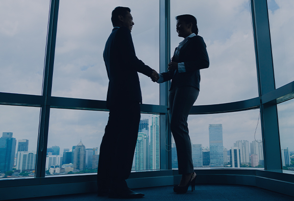 Two silhouetted professionals shaking hands in front of a large window, with a cityscape in the background.